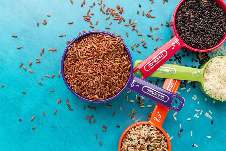 colorful image of a variety of rice in measuring cups spilling onto table